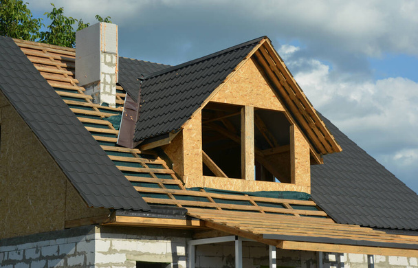 A house under construction with a close-up of the roofing construction on the stage of roof framing over a vapor barrier, metal tiles and flashing installation. Roofing Construction. - 写真・画像