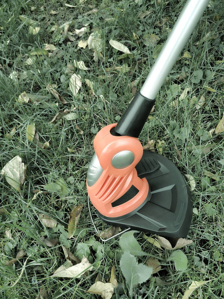 Household appliances: lawn mower-trimmer for cutting lawns on rechargeable batteries. Presented against a background of grass and leaves, front view, copy space - Foto, immagini