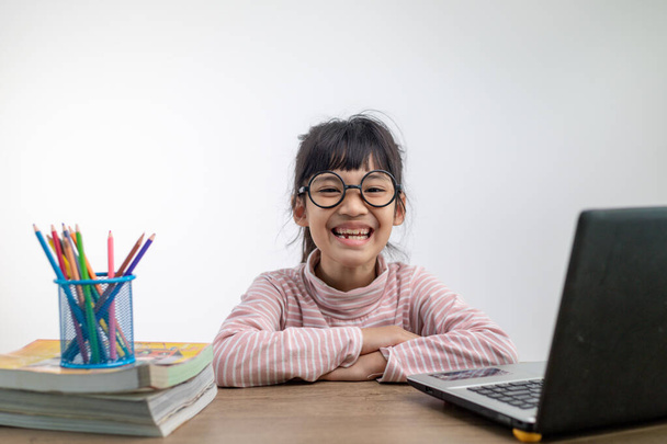 Chica asiática sentada y estudiando en casa en una computadora portátil para estudiar desde casa durante el bloqueo pandémico de Covid-19. Educación en línea, Educación en el hogar - Foto, Imagen