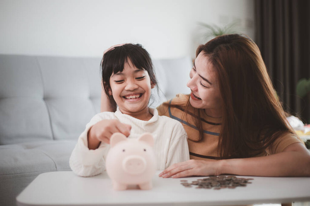 Moeder en dochter zetten munten in spaarpot. Familie budget en spaarconcept. Begrip "Junior Spaarrekening" - Foto, afbeelding