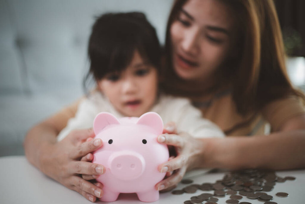 Mother and daughter putting coins into piggy bank. Family budget and savings concept. Junior Savings Account concept - 写真・画像