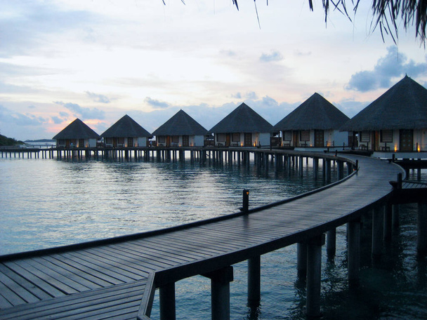 Maldives water villas in the evening - is a picture of water villas or bungalows on a perfect tropical island, in the Maldives island! The photo is perfect for projects with themes of travel, vacation, tourism, relaxation, rest, chilling, and more! - Фото, изображение