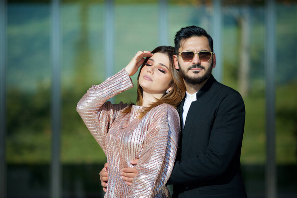 Jeune beau couple debout dans le parc sur le fond d'un bâtiment moderne. Entre un homme et une femme. Un homme avec des lunettes et une barbe. - Photo, image