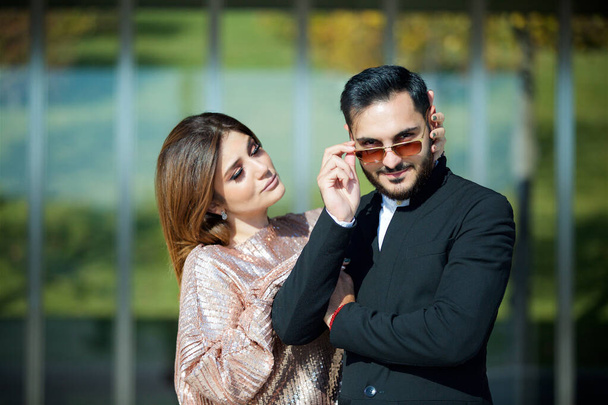 Young beautiful couple standing in the Park on the background of a modern building. Between a man and a woman feelings. A man with glasses and a beard. - Photo, Image