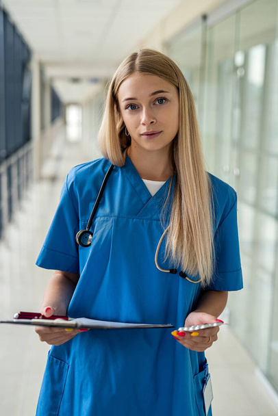 美しい看護師は聴診器とタブレットを持って廊下に立っています。医学の概念 - 写真・画像