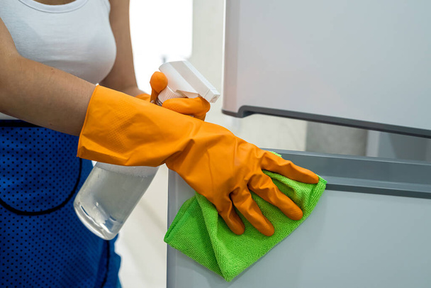 Όμορφη και ευτυχισμένη οικονόμος καθαρισμού πόρτες ψυγείο με κουρέλι . - Φωτογραφία, εικόνα
