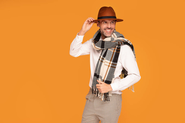 Photo of a stylish elegant handsome man posing in fashionable clothes at studio, wearing hat and scarf, smiling.  - Photo, image