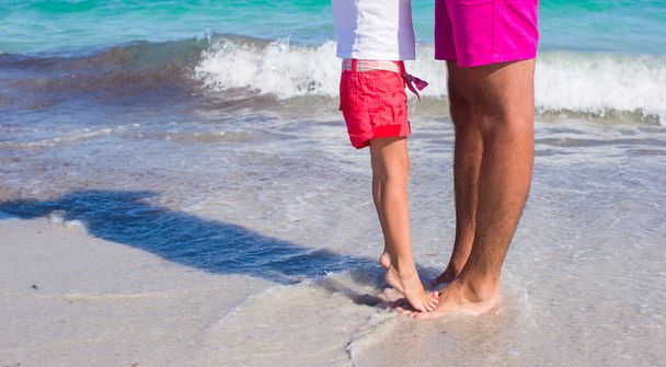 μικρό κορίτσι στέκεται στα πόδια της πατέρες στην λευκή αμμώδη παραλία - Φωτογραφία, εικόνα