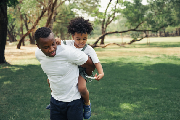 Mutlu siyahi insanlar Afrikalı Amerikalı baba parkta oynuyor ve oğlunu kucağına alıyor. - Fotoğraf, Görsel