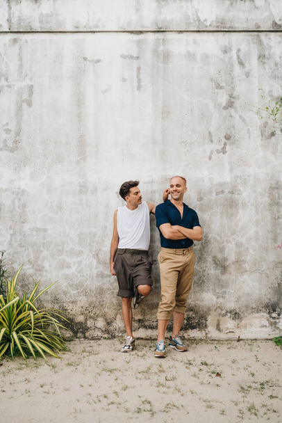 Gay Couple standing at a wall outdoors. Two men in face mask at grey wall - Photo, Image