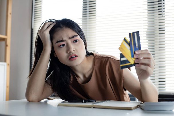 Young Asian woman is stressed and overthink by debt from many credit cards. Concept of financial problem. Women figured out a way out of debt at hand. Tired of getting into credit card debt. - Zdjęcie, obraz