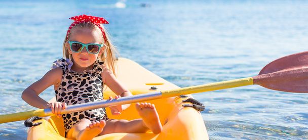 Little cute girl enjoying swimming on yellow kayak in the clear turquoise water - Photo, Image