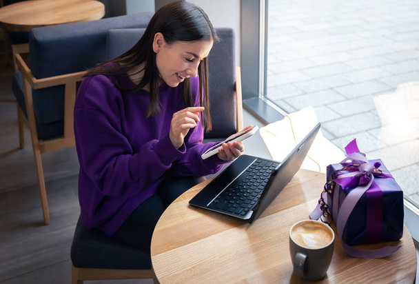 Νεαρή γυναίκα χρησιμοποιεί smartphone και laptop σε cafe, έννοια διακοπών. - Φωτογραφία, εικόνα