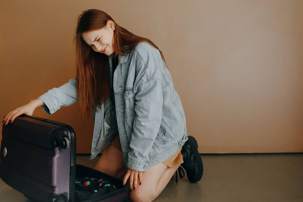 Matkustamisen käsite. Nuori nainen, jolla on matkalaukku ruskealla taustalla, valmistautuu matkustamaan - Valokuva, kuva