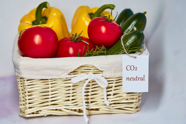新鮮な野菜にカーボンニュートラル製品ラベル付きウィッカーバスケット。炭素ラベル。ネットゼロ・カーボン排出ゼロ。地元市場からの有機農産物。新鮮なトマト、キュウリ、ピーマン - 写真・画像