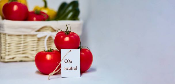 CO2-neutrales Produktetikett für Tomaten. Kohlenstoffetikettierung. Korb mit Gemüse im Hintergrund. Netto null Kohlenstoff, emissionsfrei. Biolandprodukte vom lokalen Markt. Extra breites Banner. Kopierraum - Foto, Bild