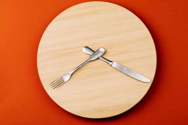 断続的な断食と食事をスキップするという概念。時計の針の形で刃物で木製の丸いトレイ. - 写真・画像