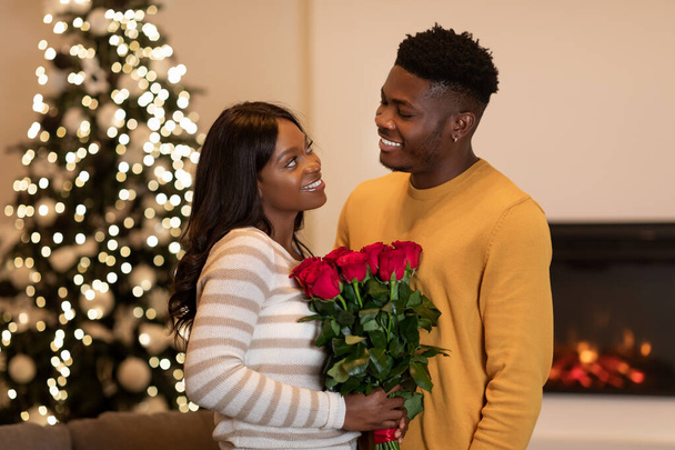 Μαύρο φίλο συγχαίροντας τη σύζυγο για το νέο έτος δίνοντας λουλούδια σε εσωτερικούς χώρους - Φωτογραφία, εικόνα