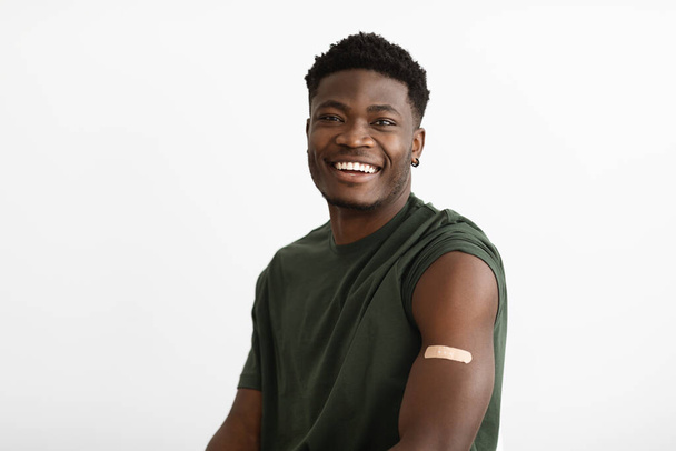 Positive handsome black man showing adhesive band on shoudler - Foto, immagini