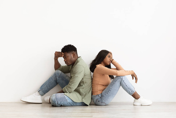 Upset african american couple sitting back to back on floor - Фото, изображение