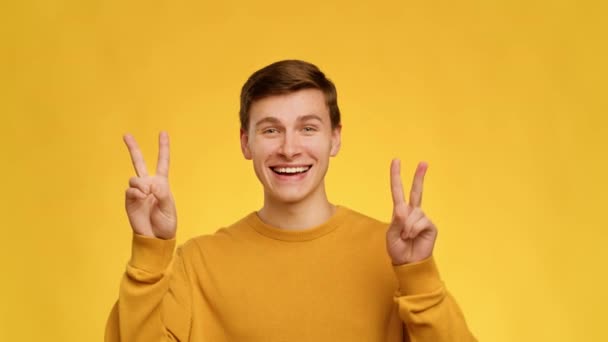 Χαρούμενος άνθρωπος χειρονομώντας V-Sign χαμογελώντας στην κάμερα πάνω από κίτρινο φόντο - Πλάνα, βίντεο