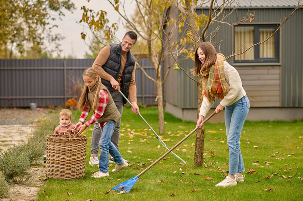 Man and woman raking leaves children near basket - Zdjęcie, obraz