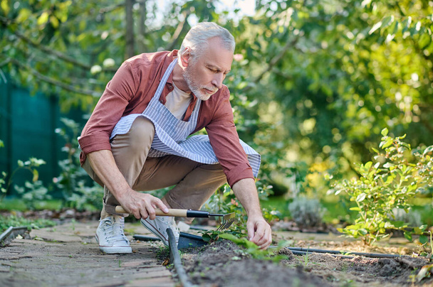 Middelbare man aan het werk in een tuin met gtareden inventaris - Foto, afbeelding