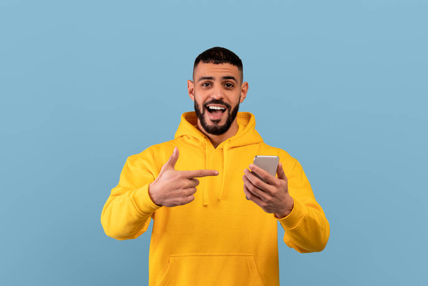 Offre mobile. Homme arabe excité pointant le smartphone dans ses mains, réagissant émotionnellement à l'application cool ou site Web - Photo, image