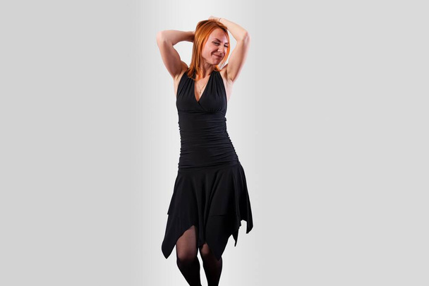 Hermosa chica en un vestido negro de nuevo bailando, sobre un fondo gris. Foto de alta calidad - Foto, Imagen