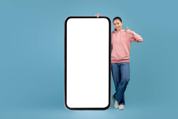 Pretty asian woman standing by huge smartphone with empty screen - Zdjęcie, obraz