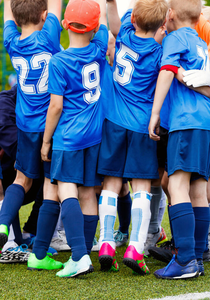 Vertical picture of happy boys in sports team celebrating success together. School kids in blue sporty jersey shirts with white numbers. Children playing sports on grass venue - Foto, afbeelding