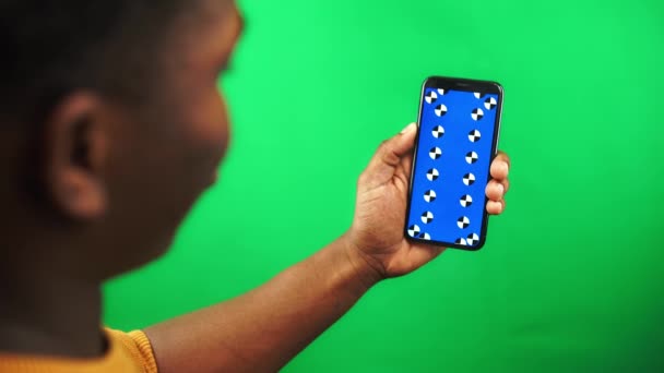 Black man is scrolling pages on smartphone with tracking markers display and green screen - Filmati, video