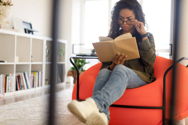 Keskittynyt musta nainen lasit yrittää lukea kirjaa - Valokuva, kuva