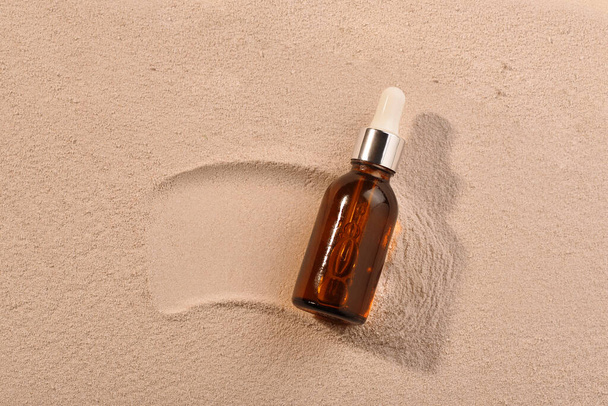 Beauty product in dark glass bottle on sand background with sunlight and shadow. Serum oil. Flat lay - Foto, imagen
