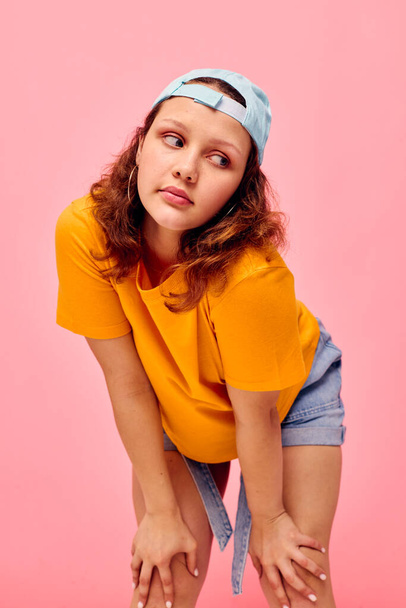 beautiful woman in a yellow t-shirt and blue cap posing emotions pink background unaltered - Photo, Image