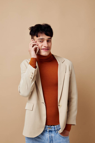 portrait of a young man in a beige jacket talking on the phone light background unaltered - Foto, Imagem