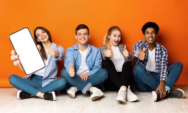 Group Of Teens Sitting On Floor And Demonstrating Blank Smartphone, Mockup - Photo, Image
