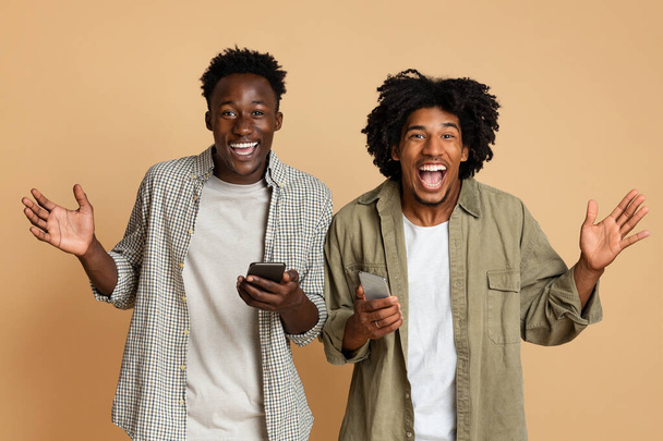 Mobil Teklif. Ellerinde akıllı telefonlar olan iki heyecanlı siyahi arkadaşın portresi - Fotoğraf, Görsel