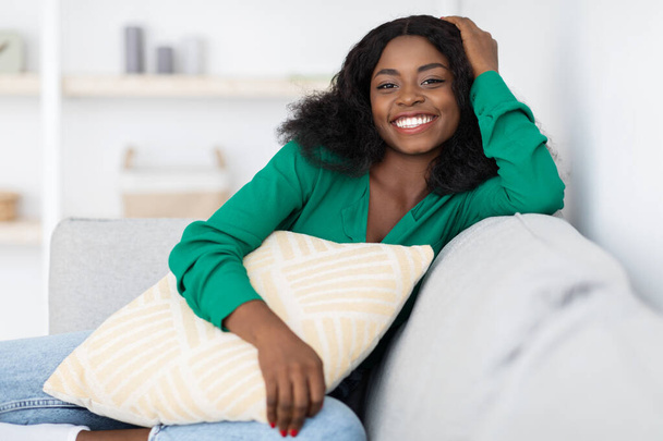 Sonriente mujer afroamericana bastante sentada en el sofá en casa - Foto, Imagen
