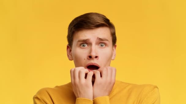 Scared Guy Biting Nails Looking At Camera Over Yellow Background - Imágenes, Vídeo