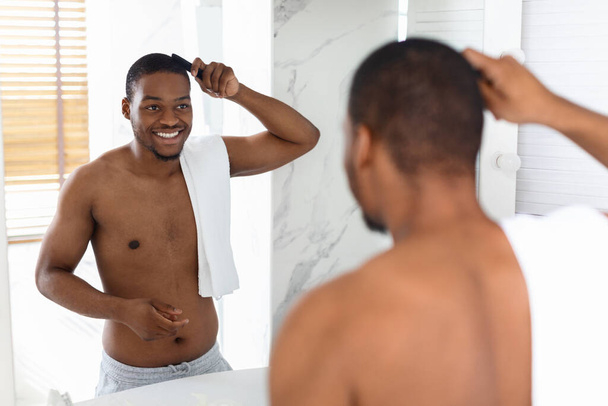 Handsome Shirtless Black Man Combing Hair And Looking In Mirror In Bathroom - Foto, Imagen