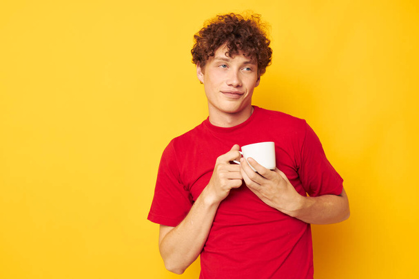 guy with red curly hair in a red T-shirt with a white cap in his hands isolated background unaltered - Foto, imagen