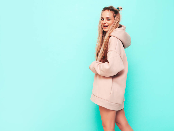 Young beautiful smiling female in trendy summer hoodie. Sexy carefree woman posing near blue wall in studio. Positive blond model having fun and going crazy. Cheerful and happy - Photo, image