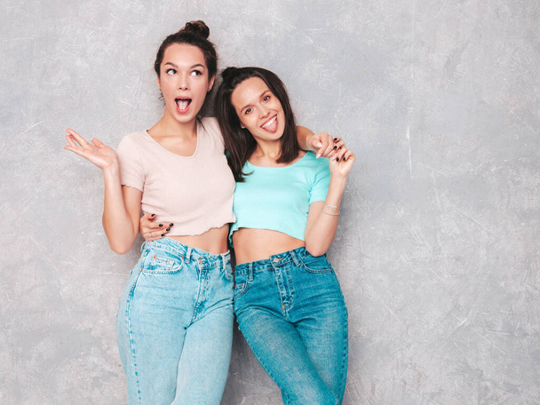 Two young beautiful smiling blond hipster female in trendy summer clothes.  carefree women posing near grey wall in studio. Positive models having fun. Cheerful and happy.they show tongues - Fotoğraf, Görsel