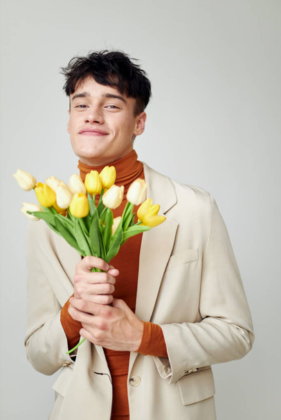 pretty man in white jacket with a bouquet of yellow flowers elegant style model studio - Zdjęcie, obraz