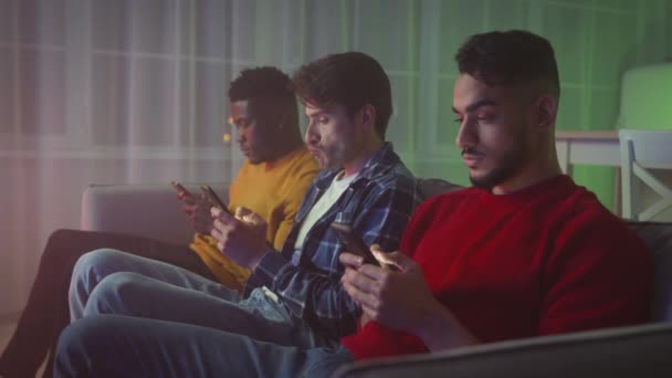 Problems of modern communication. Three multiethnic young men web surfing in social media on phones, ignoring real talk - Materiaali, video