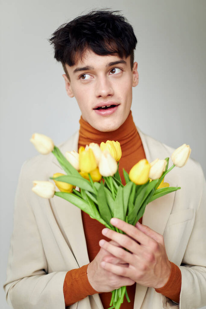 A young man in white jacket with a bouquet of yellow flowers elegant style background unaltered - Photo, Image