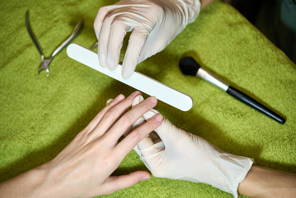 Woman in salon receiving manicure by nail file. - Фото, изображение