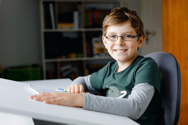 A szemüveges kisfiú otthon tanul az iskolába. Színlelt gyerek házi feladatot csinál. Otthoni oktatás és távoktatás koncepciója. - Fotó, kép