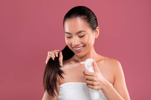 Uzun saçlı mutlu Asyalı kadın saç spreyi kullanıyor. - Fotoğraf, Görsel